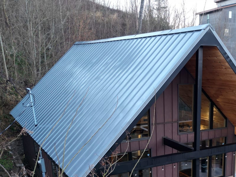 Three-quarter aerial of the A-frame cabin with the full sweep of its ribbed metal roof running down to the eave