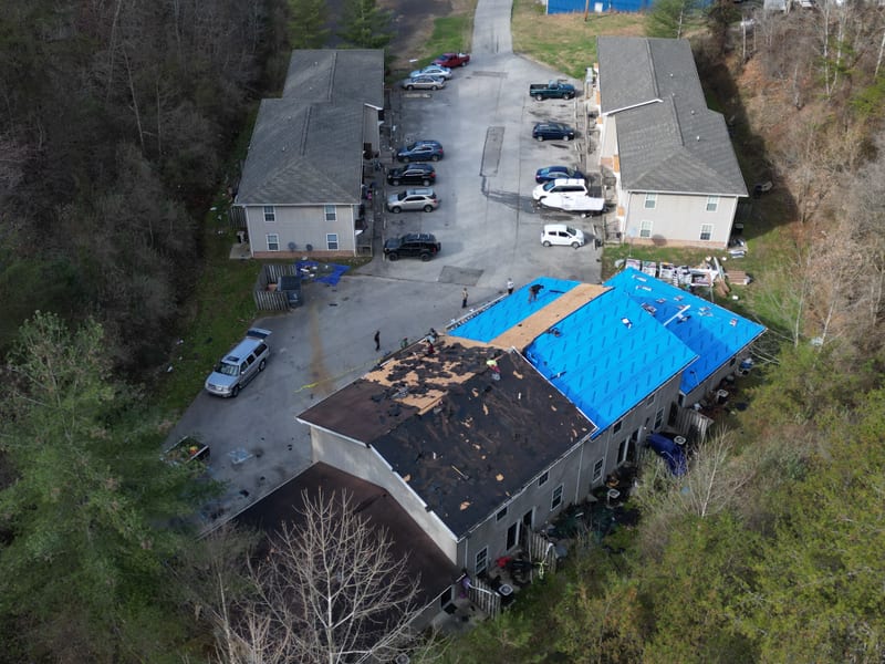 Complex-wide aerial mid tear-off with old shingles stripped and blue underlayment going down