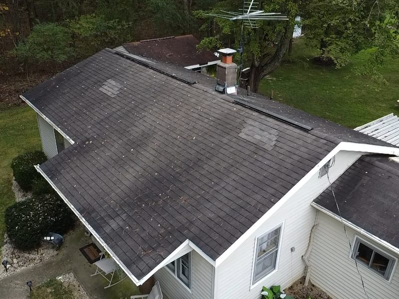 Drone view of the original roof: worn, curling three-tab with several mismatched lighter patch repairs