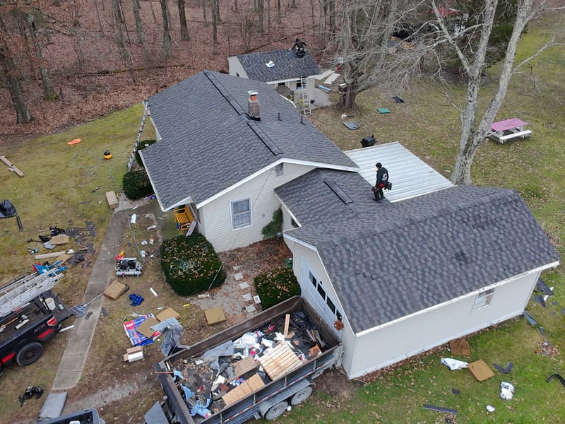 Working shot with the new roof mostly laid, dump trailer backed to the garage and heaped with tear-off