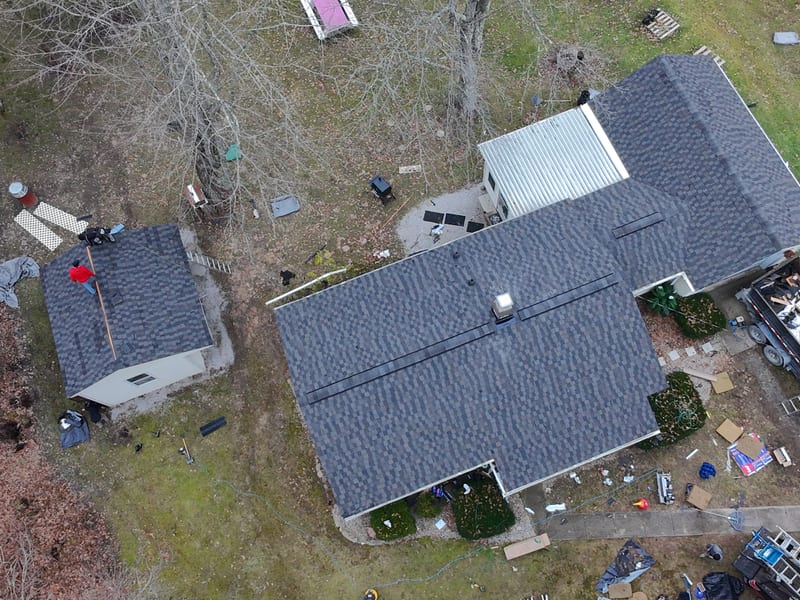 Whole-property view from above: house and attached garage finished in new laminate shingle, the detached outbuilding under way