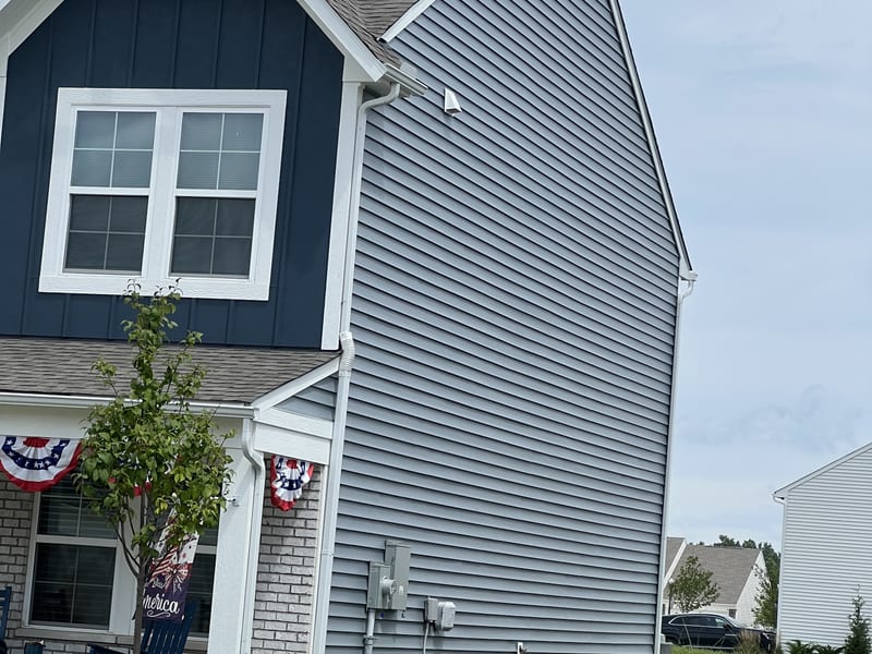 Two-story home with navy board-and-batten gable and blue vinyl siding, repaired wall lying flat