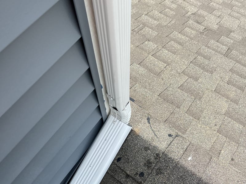Close-up of a gutter corner miter and downspout outlet against gray vinyl siding