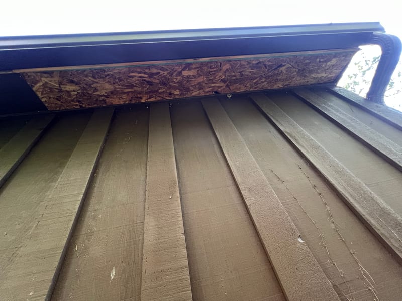 Soffit underside with the raw deck edge left exposed above the gutter where the sub-fascia should close it in