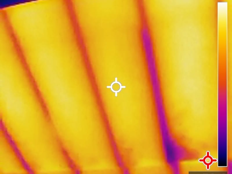 Thermal camera image of attic rafter bays glowing yellow and orange, with the temperature color scale on the right