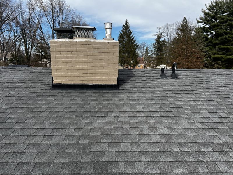 New pipe boots and vents along the freshly shingled slope, with the repainted chimney and its new caps behind