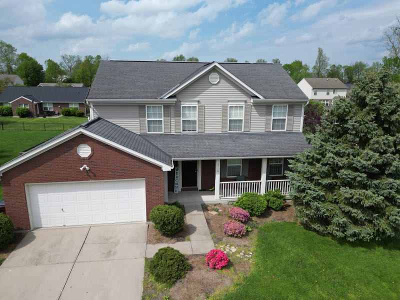 Elevated drone view of the finished colonial, fresh shingle planes over the brick front and attached garage
