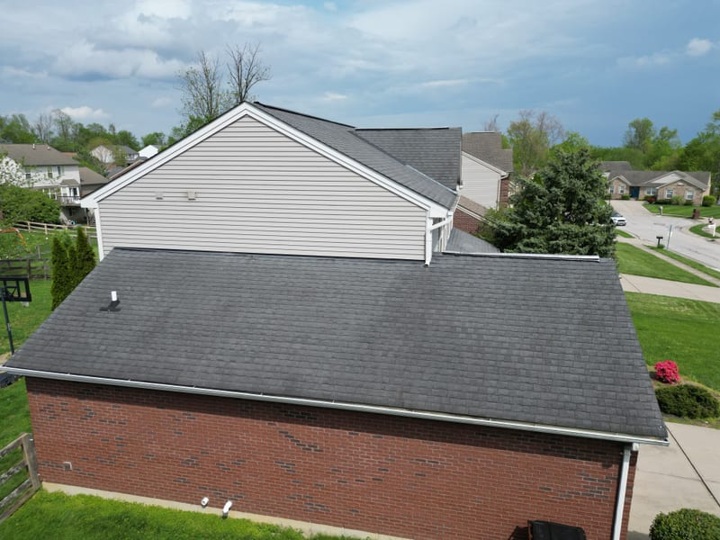 Rooftop-level view across the garage wing of the same colonial, clean new shingle courses in spring sun