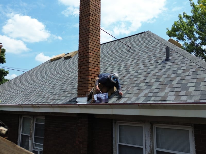 Crew member sealing new chimney flashing at the ridge of the freshly shingled designer-blend hip roof