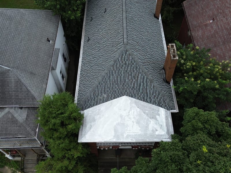 Overhead drone view of the finished designer-blend shingle roof on a brick Tudor duplex with relined box gutters and coated porch roof
