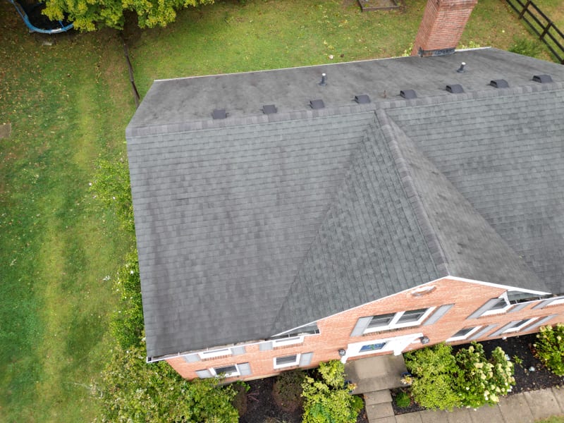 Overhead drone view of the finished brick two-story, chimney and full roof plane in frame