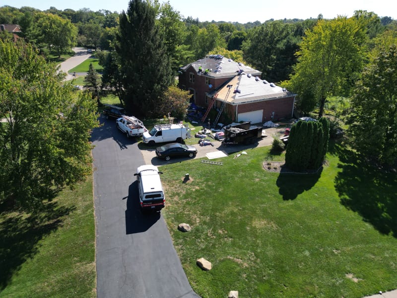 Wide aerial of the job site with the crew spread across the felt-covered roof and trucks staged below