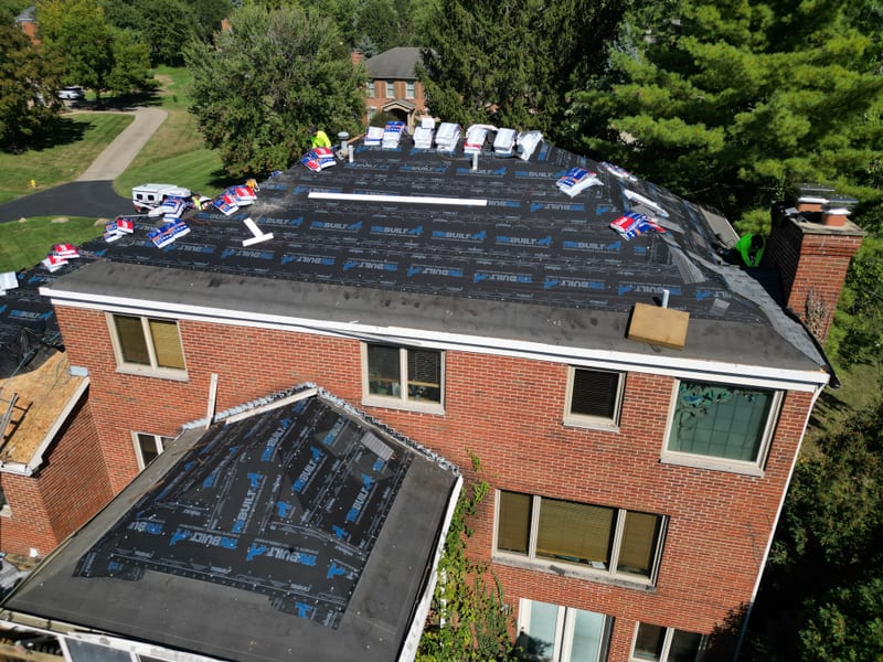 The main roof plane fully wrapped in synthetic underlayment with shingle bundles staged along the ridge