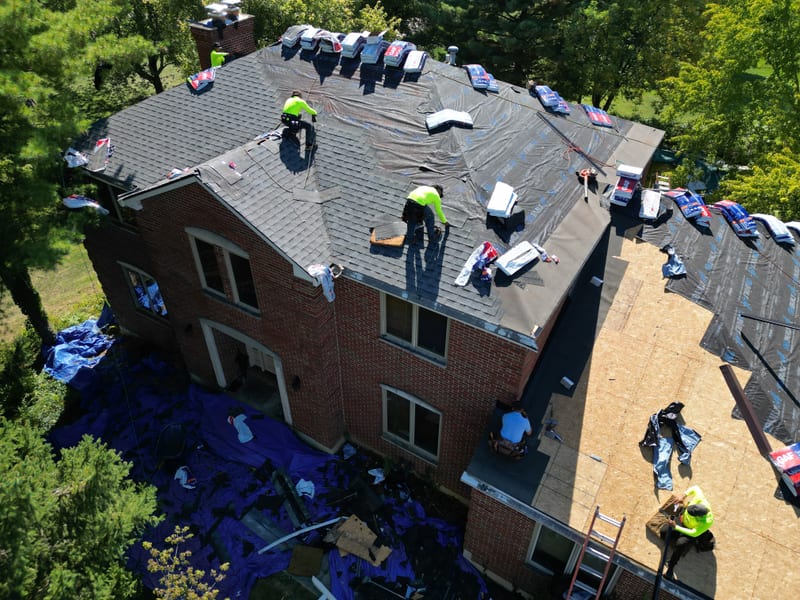Five crew members mid tear-off across three roof sections as old shingles come off