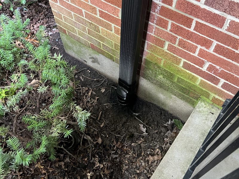 Downspout base connector tied into the underground drain line at the foundation of a brick home