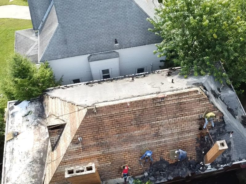 Drone view of the crew stripping two layers of shingles down to plank decking on a two-story hip roof