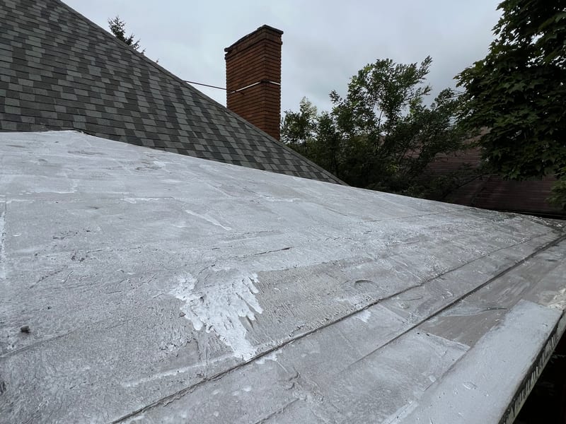Freshly silver-coated flat roof section in front of the new architectural shingle slope and brick chimney