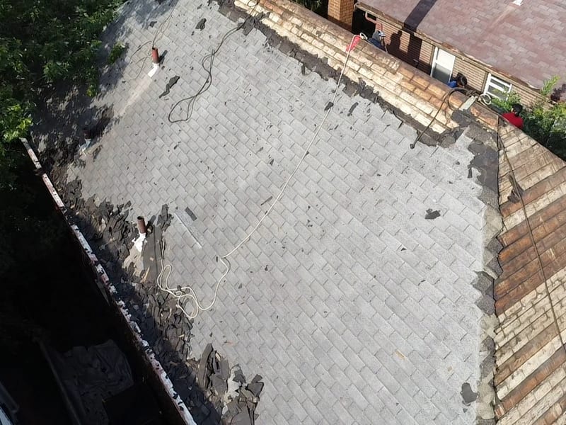 Drone overhead of the shingle field mid-strip with torn debris along the eaves and decking opening up at the ridge