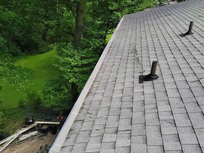 New seamless gutter with mesh screens running the full eave of a home surrounded by woods, seen from the roof