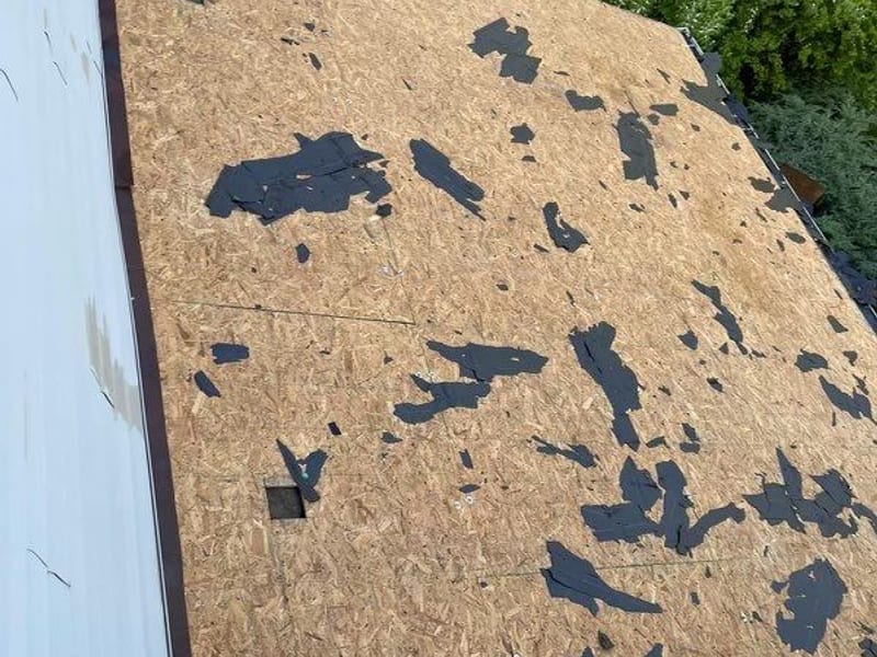 The deck stripped to bare sheathing and scattered with torn-off asphalt, hillside back yard below