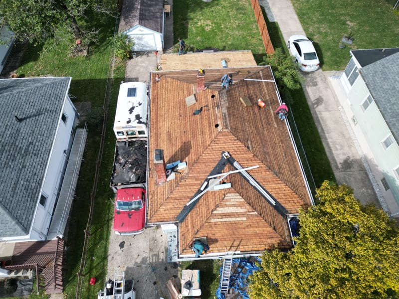 Oblique aerial with the entire hip roof stripped to its original board sheathing, bare planks running the full field