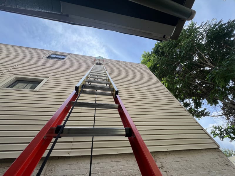Technician at the top of the long extension ladder working the loose siding piece back into place