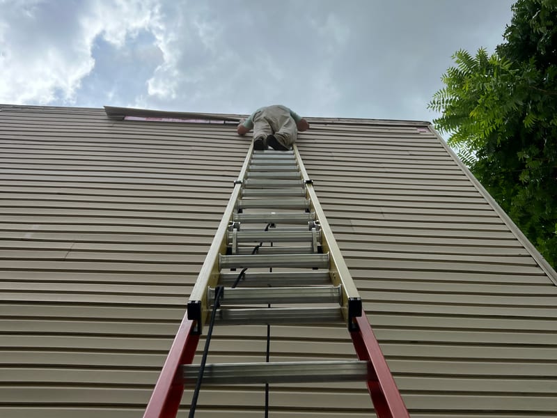 Two extension ladders set side by side against the tall tan gable during the repair