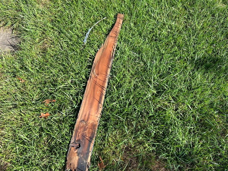 Removed length of rotted wood trim laid on the grass, showing split and decayed wood along its length