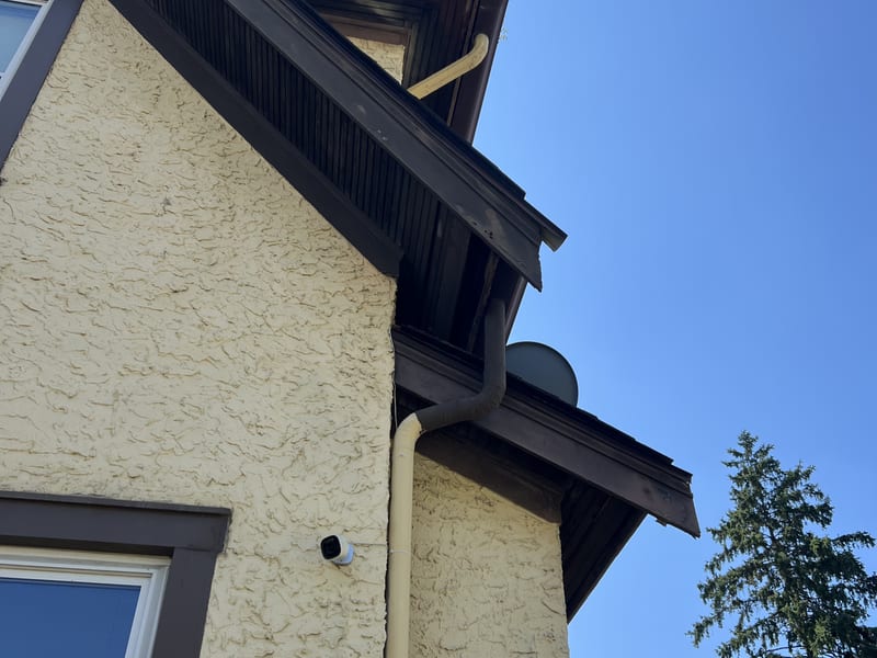 Cream stucco two-story shot from the ground, the damaged overhang visible at the roof line