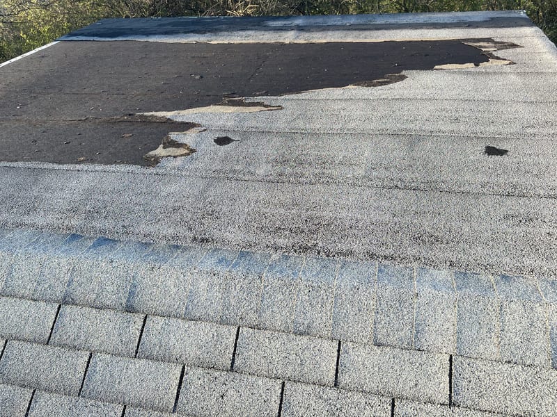 Wind-stripped low-slope roof section with the mineral-surfaced roll roofing peeled back in a large ragged sheet