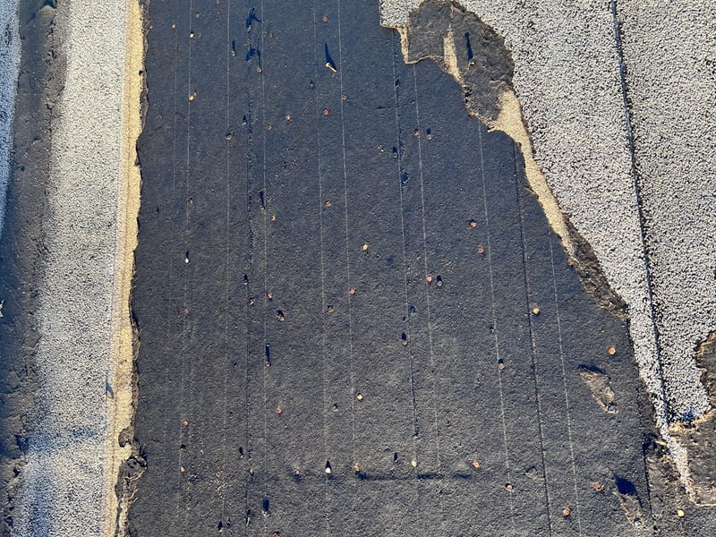 A section of roll roofing torn clean away, bounded on both sides by intact granulated surface