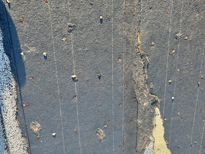 Close view of the torn edge with exposed felt, scattered backed-out nails and the decking board lines showing through