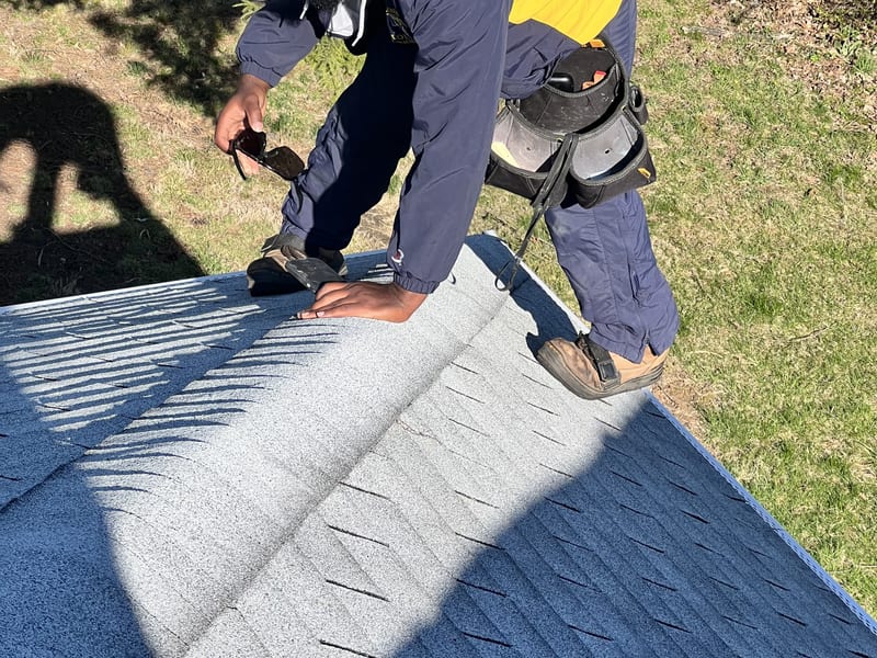 Crew member on the ridge lifting away a storm-loosened ridge cap shingle