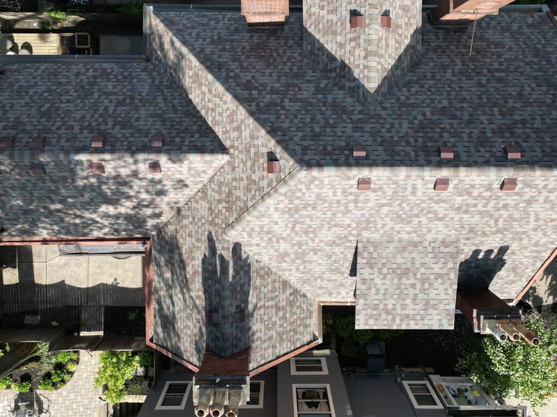 Top-down drone view of the finished roof across the whole cruciform footprint in new multi-tone shingle