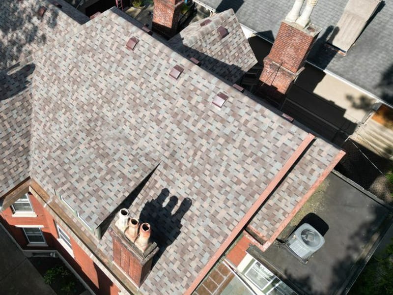 Oblique aerial of the finished roof plane and chimneys, set against a neighbouring weathered grey roof