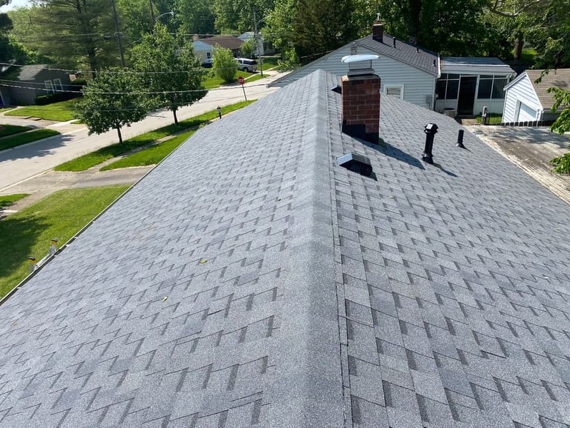 The finished roof from the ridge in full sun, new grey shingles running the length of the house past the brick chimney
