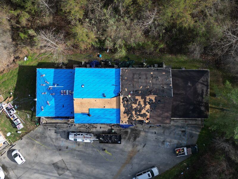 Aerial drone view of apartment building mid-tearoff with blue underlayment and crew working