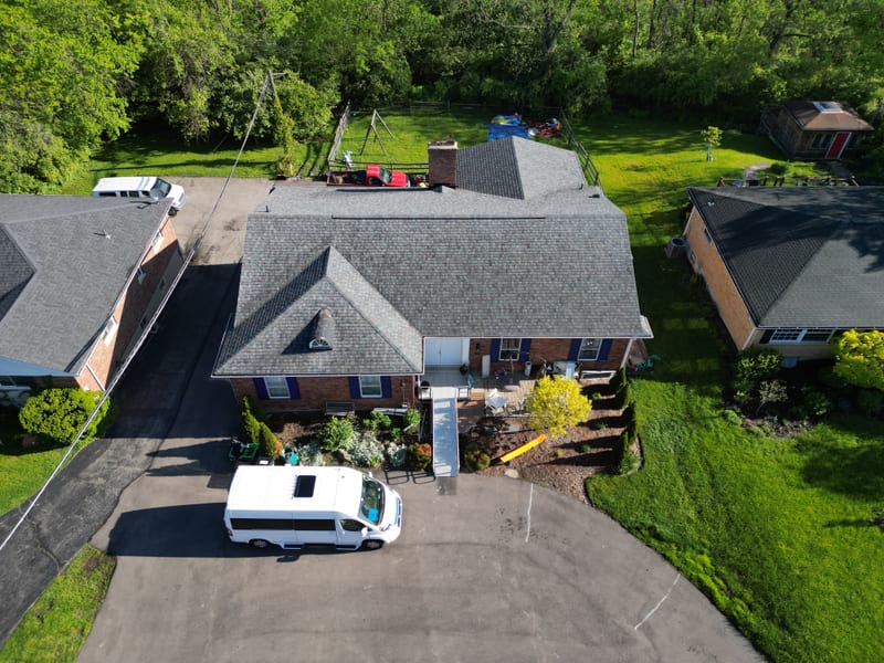 Three-quarter aerial of the completed roof in morning sun, new designer-blend shingles on every plane