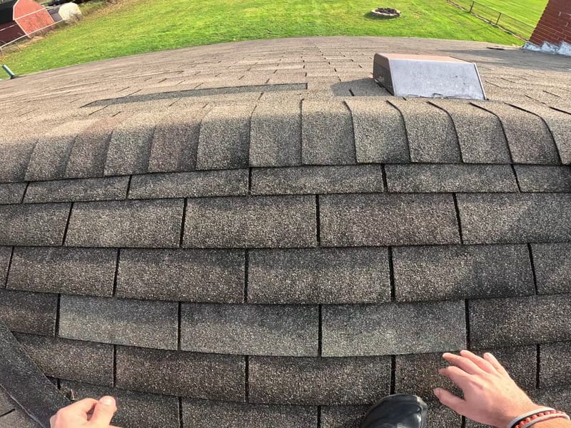 Chest-camera view down onto the hip as new shingles are woven into the existing courses