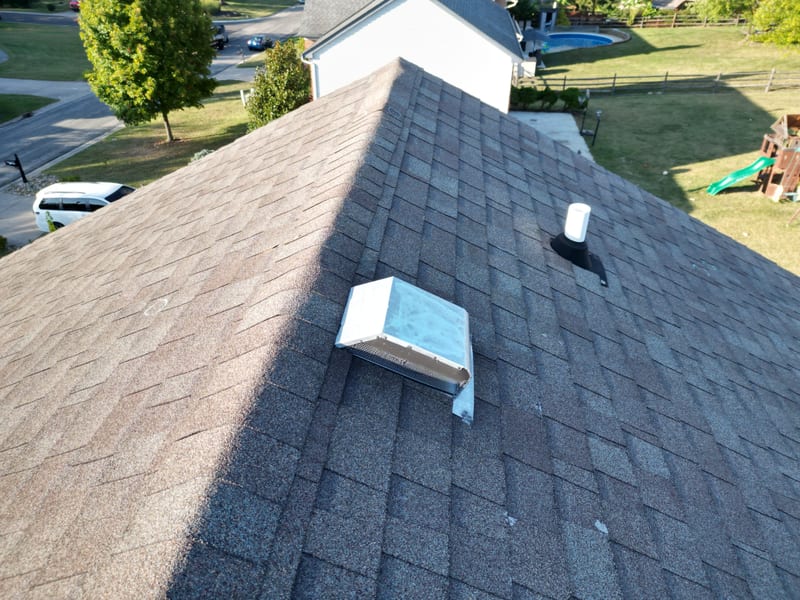 Ridge view of the hail-inspected roof showing a box vent, pipe boot and chalk-marked impact