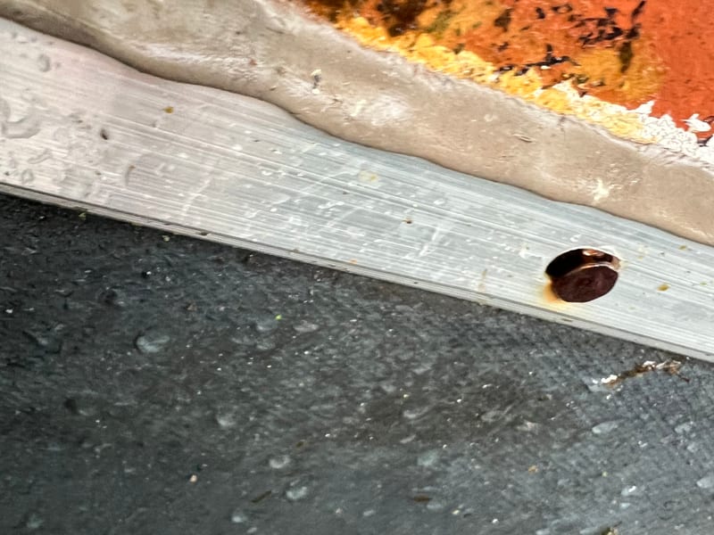 Metal step flashing bedded in a continuous sealant bead where a flat EPDM roof meets brick masonry, photographed wet after rain