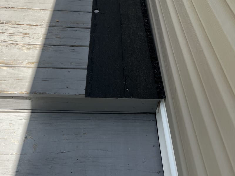 Removed asphalt shingle sample strips laid flat on gray-painted porch decking against the home’s light siding, staged for warranty-claim documentation