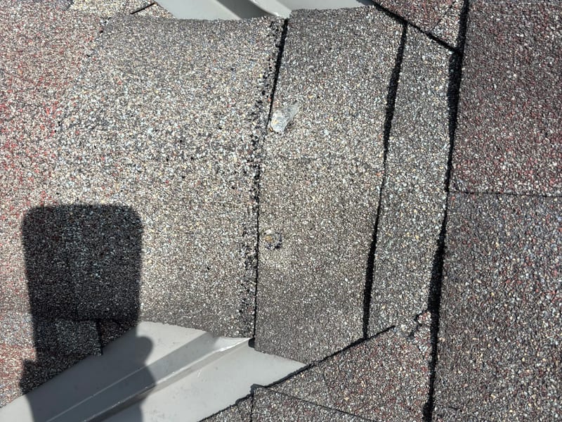 Roof detail of a shingle patch between two metal flashing runs, with fresh sealant along the shingle seam
