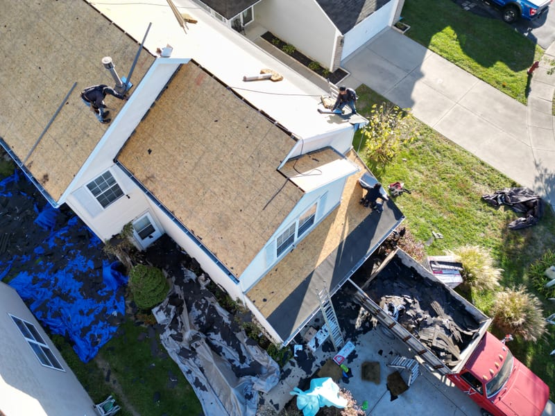 Tear-off complete with the roof down to bare sheathing across every plane, ground fully tarped and the debris truck loaded