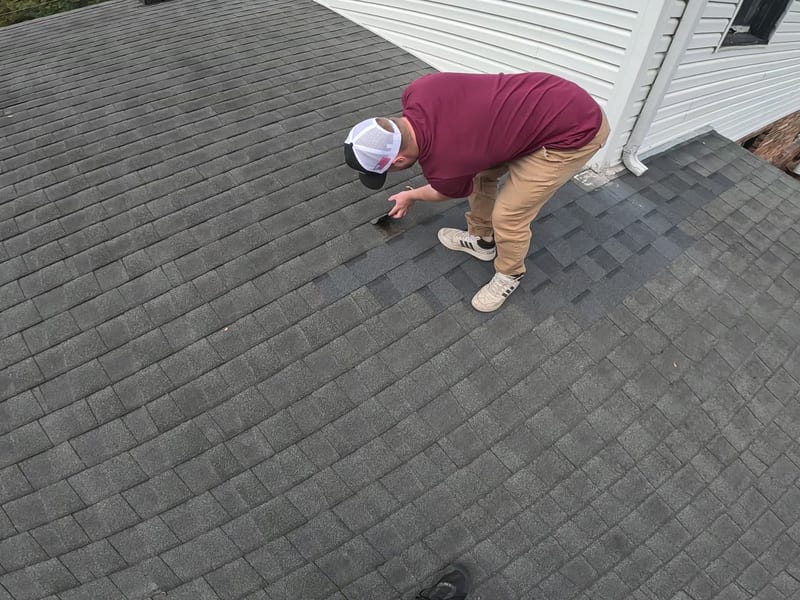 Wide view of the roof plane as a technician fits fresh replacement shingles into the wind-damaged section