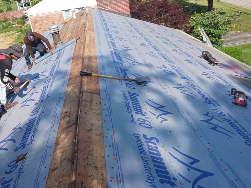 Crew laying underlayment with the ridge still open, the original ridge board and old decking visible