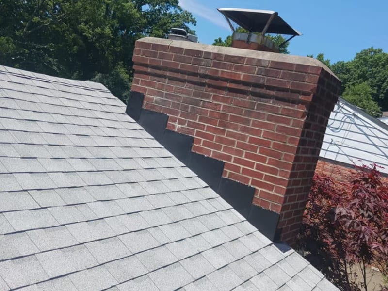 New black step flashing stepped cleanly up the corbelled brick chimney against the finished light grey field