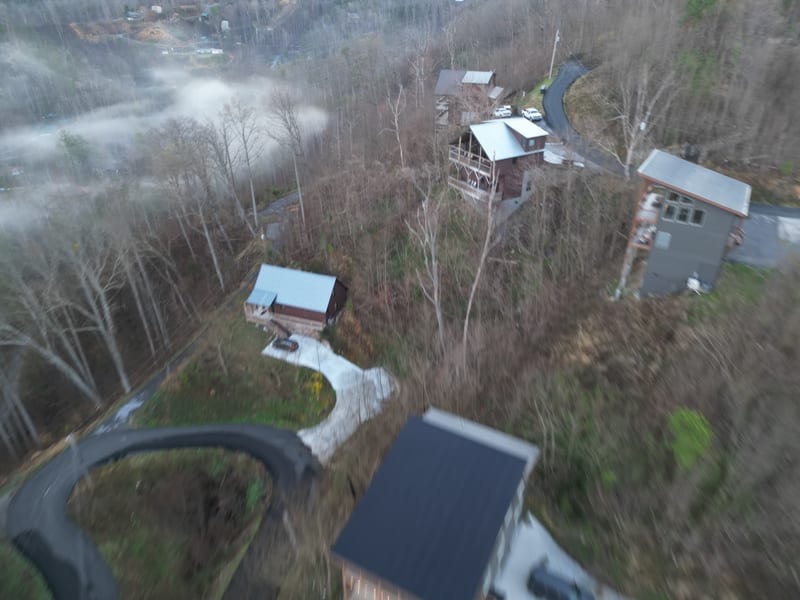 Aerial view of the cabin community on the misty mountainside, metal roofs among the bare trees