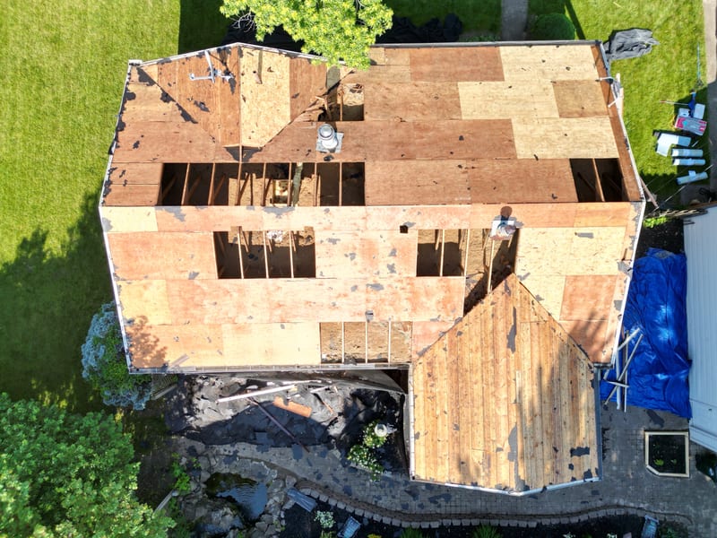 Full-property view showing the stripped deck, open rafter bays, tarped landscaping and staged materials