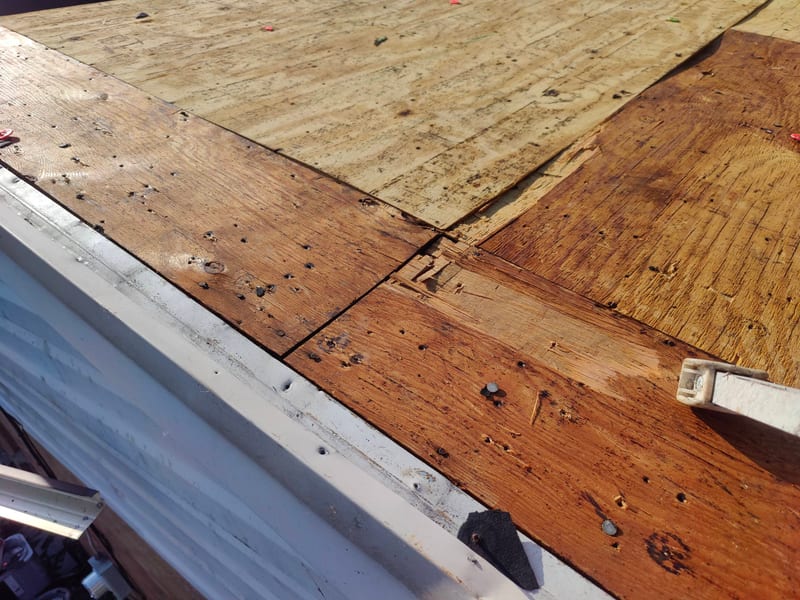 Eave-level view of the stripped edge where the old nail-riddled plank deck meets the existing trim